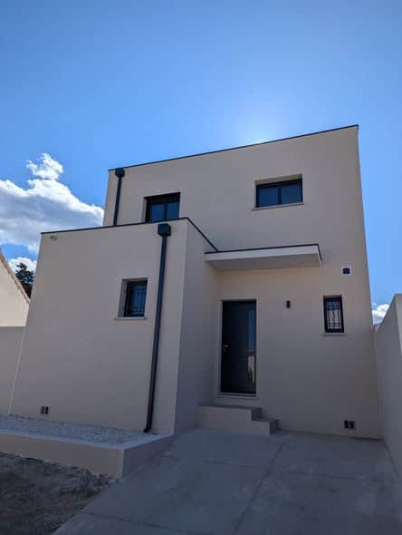 Maison Moderne à Toit Plat et Façade Beige Épurée Maison contemporaine à toit plat avec façade beige épurée et menuiseries noires sous un ciel bleu.