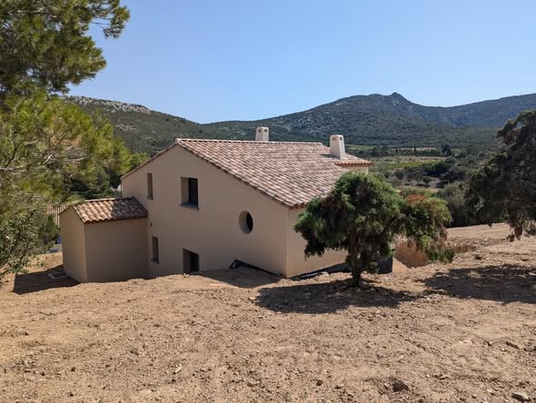 Architecture Provençale : Maison avec Vue sur les Collines Maison contemporaine aux murs beige et toit de tuiles dans un paysage méditerranéen vallonné.